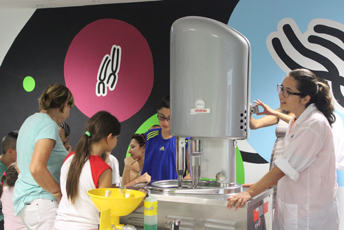 Children and adults during an activity at the museum. A museum instructor in a white lab coat stands in front of them