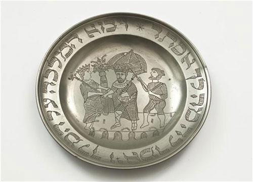   Tin Purim plate. In the middle an engraving of the king and two servants, and around the rim - a verse from the Esther Scroll.