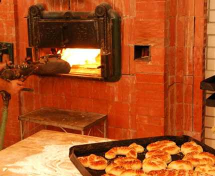   A large brick bakery oven with a fire burning inside. On a table is a tray with loaves of fresh bread