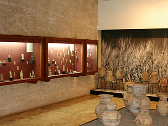 An exhibition hall with ancient pottery on the floor and ancient items in glass display cabinets on the wall